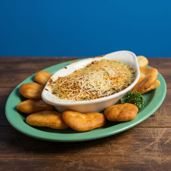 Baked spinach dip with melted cheese and golden brown bread pieces on a green plate.