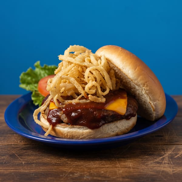 A BBQ cheeseburger topped with crispy fried onions, lettuce, and tomato on a blue plate.