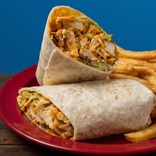 Two chicken wraps with lettuce and sauce, served with fries on a red plate.