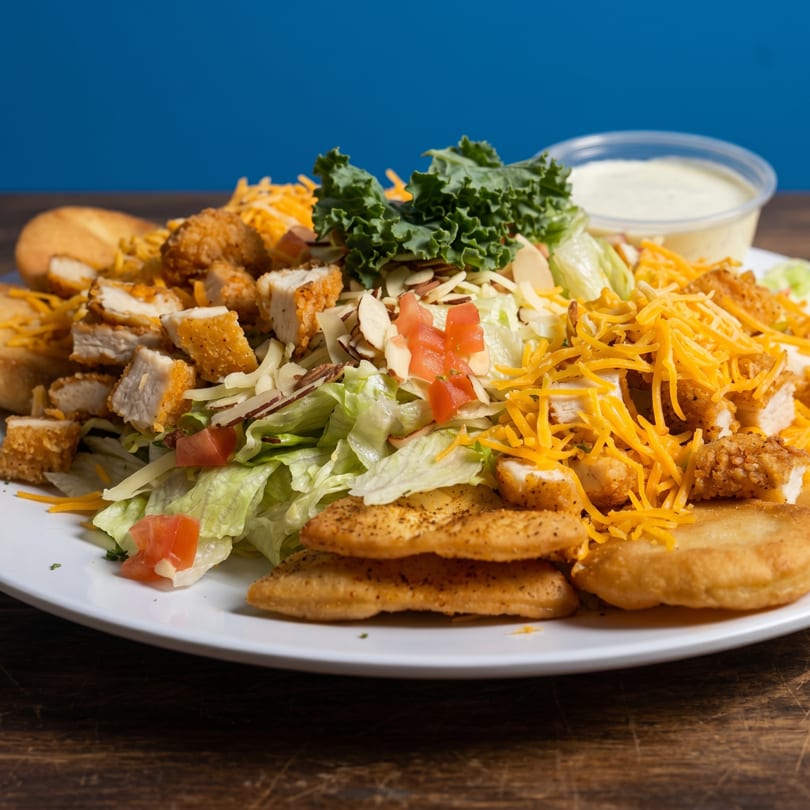 A large salad with fried chicken, shredded cheese, lettuce, tomatoes, and almonds on a white plate.