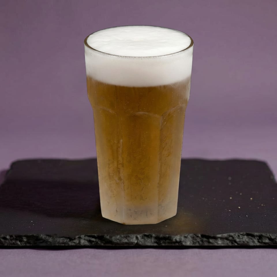 A frosty glass of beer with a thick head of foam sits on a dark slate coaster.