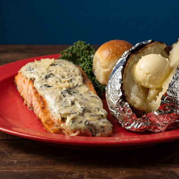 Grilled salmon with creamy sauce, a foil-wrapped baked potato with butter, and a dinner roll.