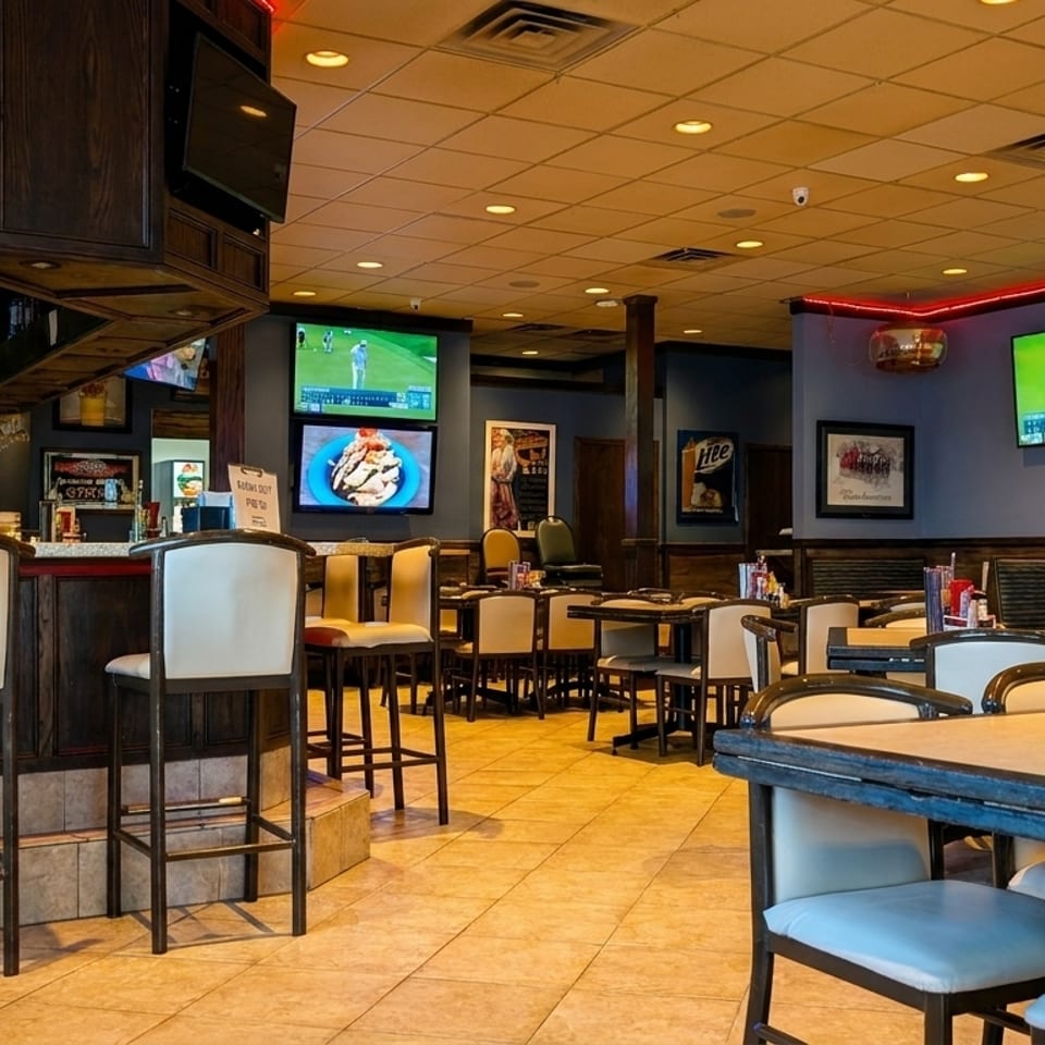 Interior of a sports bar with multiple TVs showing golf, a long bar, and dining tables.