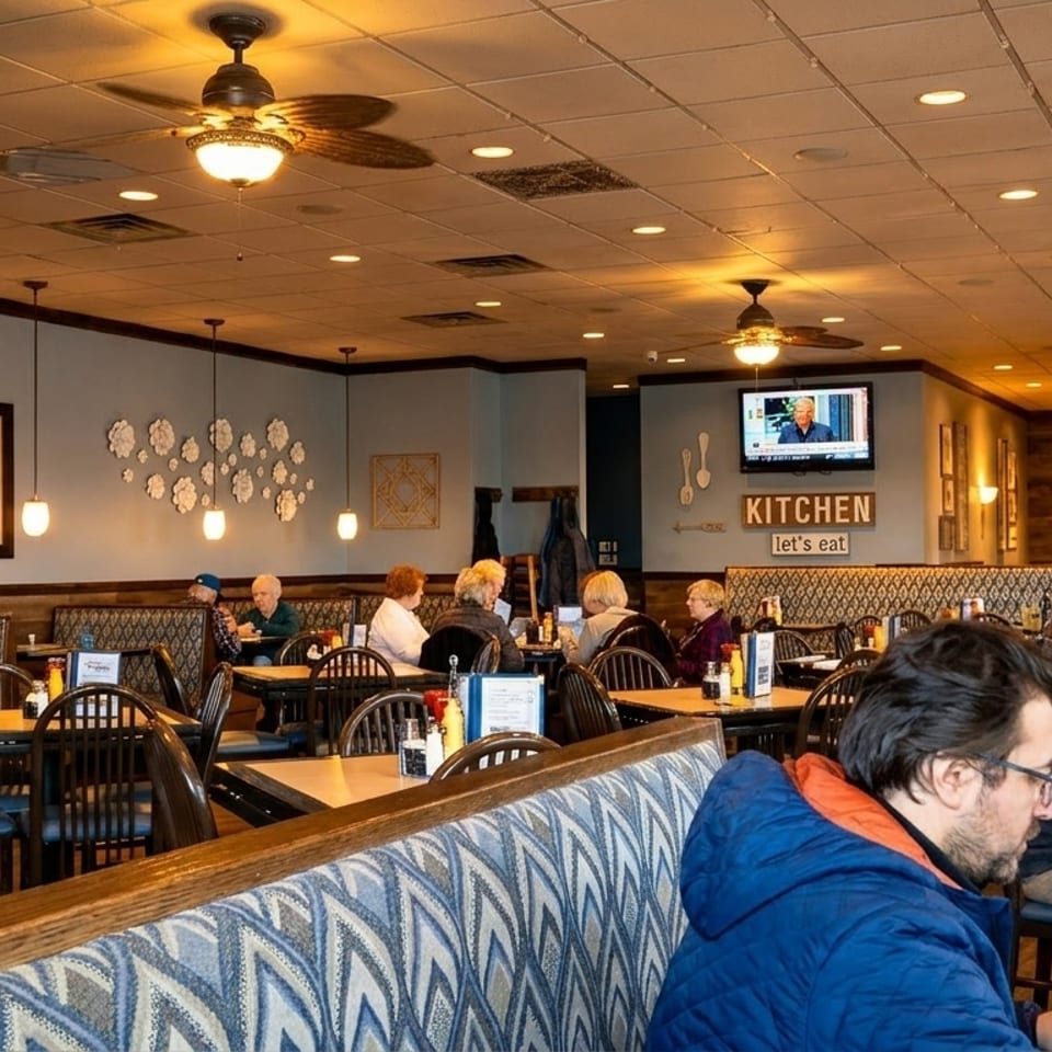 Diners seated at tables and booths in a brightly lit, casual restaurant with TVs and decorative wall art.