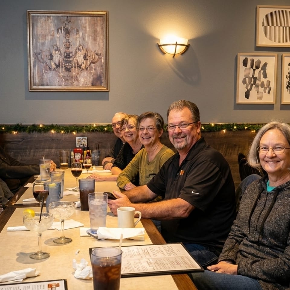 Group of eight smiling people seated at a long table in a restaurant, enjoying drinks.